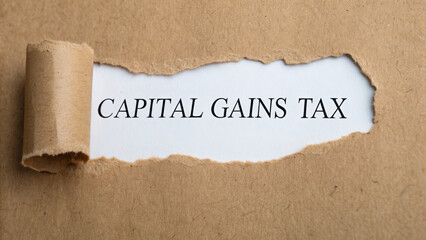 Capital gains tax business finance goals capital gains tax phrase revealed under torn paper expressing financial planning and business goal focus with thoughtful mood