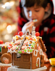Young child eating candy with gingerbread house in foreground