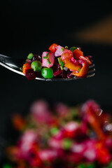 Fork with colorful beetroot salad close-up, healthy vegan meal on dark background