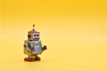 Cute retro tin robot toy standing on yellow background, symbolizing vintage technology, innovation, and playful creativity in a minimalistic and nostalgic concept design scene.