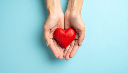 Fototapeta premium Hands Cradle a Red Heart Symbolizing Affection and Kindness on a Blue Background