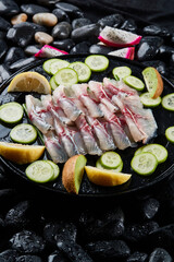 Arrange the glistening, white slices of fresh fish on a black round porcelain plate.