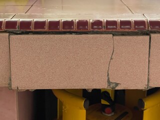 Close-up of a cracked pink ceramic kitchen countertop tile with rough repair line and aging...