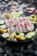 Arrange the glistening, white slices of fresh fish on a black round porcelain plate.