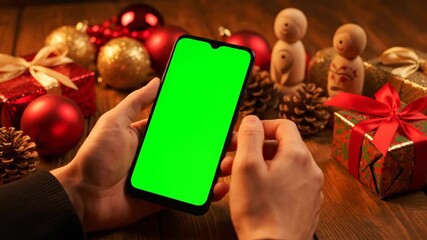 Close-up shot of hands holding a smartphone with a green screen, festive background. - Powered by Adobe