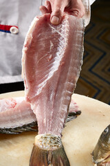On a white cutting board, the chef demonstrates his exquisite knife skills in cutting and slicing sashimi and fresh fish.