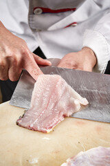 On a white cutting board, the chef demonstrates his exquisite knife skills in cutting and slicing sashimi and fresh fish.