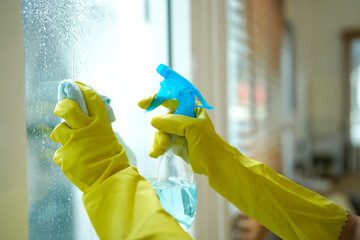Person wearing yellow gloves cleaning a window with a spray bottle and cloth