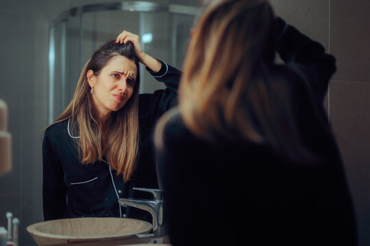 Woman Looking in the Mirror Checking the Roots of her Hair. Lady feeling insecure about her hair looking for bald spots 