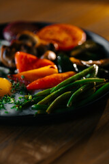 Close-up of breakfast with fried eggs, grilled vegetables and green beans on dark plate