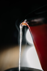 Close-up of pouring hot herbal tea from glass teapot with steam