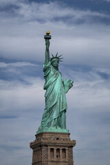 Fototapeta premium Iconic green monument of a woman holding a torch, standing on a stone pedestal against a cloudy sky in New York City.