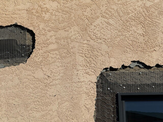 Close-up view of exterior stucco wall under repair with exposed wire lath and nails showing structural layers of cement and insulation on a residential building facade