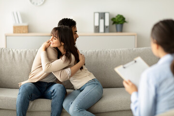 A happy arab couple embraces in a counselor's office after completing successful marital therapy. They express gratitude to their psychologist, showing relief and joy in saving their marriage.