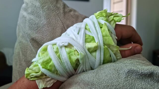 Someone's hand is wrapped or bandaged with lettuce and has a pain-relieving effect.