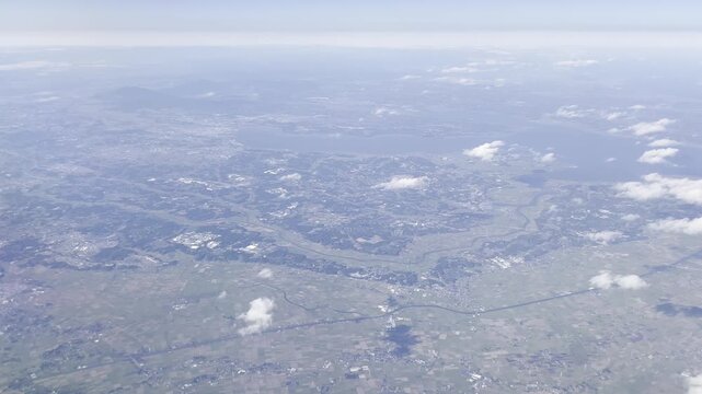 View from airplane window flying over Japan &ndash; clouds and mountain landscape under clear blue sky
