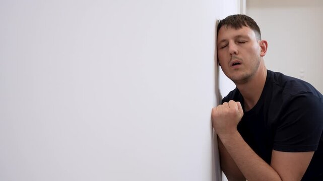 Hopeless depressed caucasian man bang against white wall dealing with PTSD