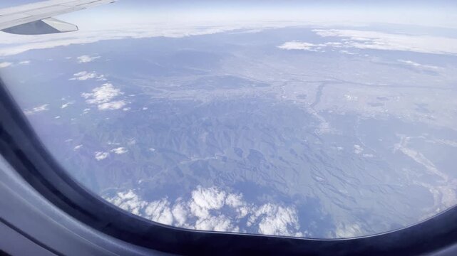 View from airplane window flying over Japan &ndash; clouds and mountain landscape under clear blue sky
