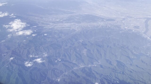 View from airplane window flying over Japan &ndash; clouds and mountain landscape under clear blue sky
