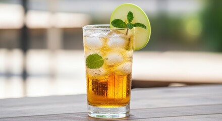 A refreshing amber-colored drink with ice, mint, and a green apple slice in a tall glass.