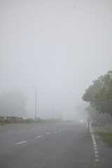 Cars drive through dense fog on a misty morning road
