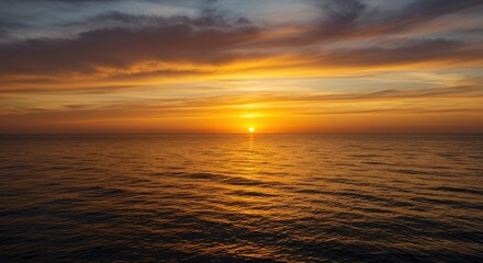 Naklejka premium Dramatic golden hour colors paint the vast sky above the calm ocean horizon as the sun dips below the water line creating a stunning view ,dusk ,colorful ,orange