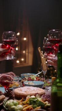 Vertical slow motion video moving camera over festive table friends making toast with red wine glasses concept thanksgiving dinner christmas celebration family gathering cozy home atmosphere