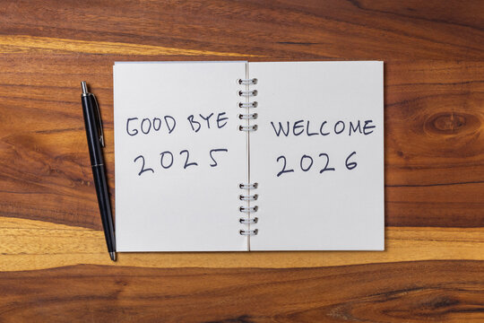 A notebook with the words "Good bye 2025, Welcome 2026" written on it, lying on wooden table