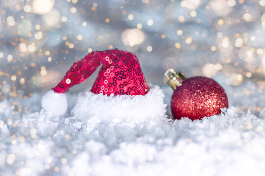 Santa hat and red Christmas ornament in snowy scene with warm glow and bokeh lights - Powered by Adobe