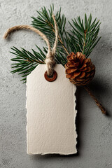 Close-up of a blank tag with torn edges with a pine branch and a pine cone on a gray background
