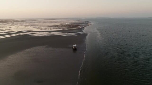 Lateral aerial of a boat sitting at low tide near a curved sandbar with gentle ripples. Wadden Sea.