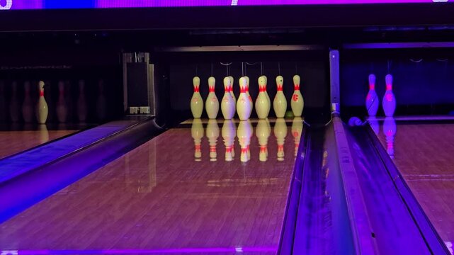 Fixed shot of bowling pins as the ball rolls down the lane and falls into the gutter.