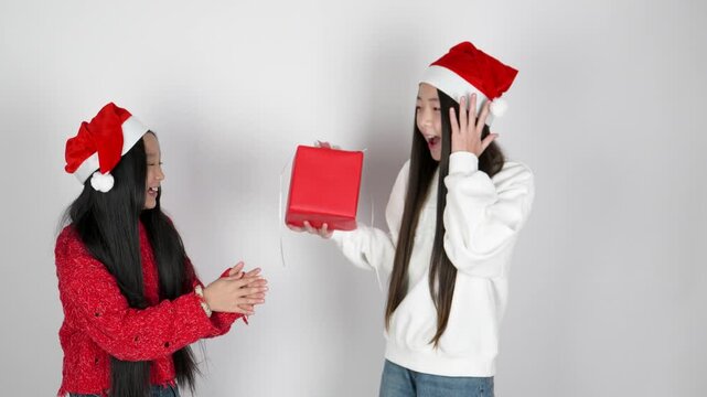 Two little girls wearing Santa hats are exchanging a red gift box