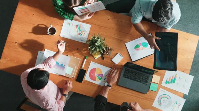 Top down aerial view of business man pointing and presenting at financial chart while diverse team discussing about stock market statistic at meeting table with laptop and graph document. Convocation. - Powered by Adobe