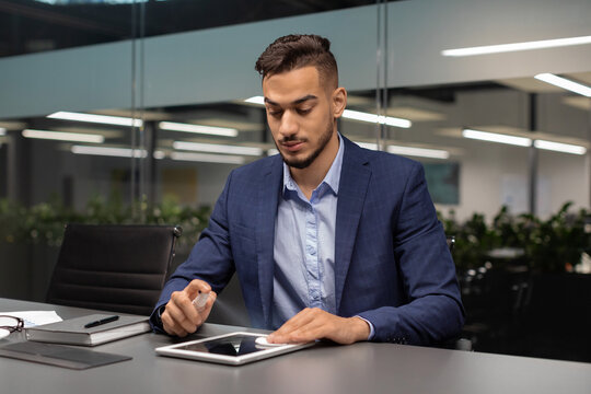 Handsome middle eastern businessman is using alcohol gel and a cotton pad to clean a digital tablet screen.