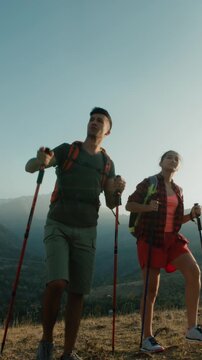 vertical slow motion cinematic video of young couple hiking in bright mountain landscape man pointing to peak symbolizing freedom unity mindfulness adventure lifestyle and romantic travel spirit