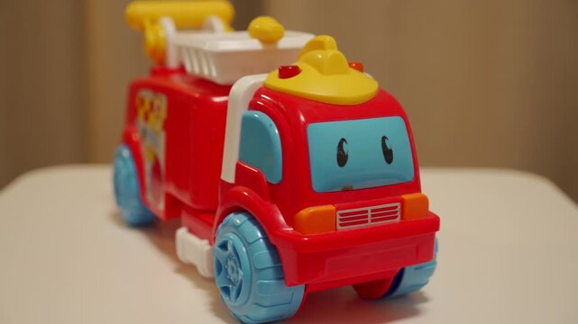 A red plastic toy truck flashes its roof light. The animated vehicle plays a cheerful, upbeat melody.