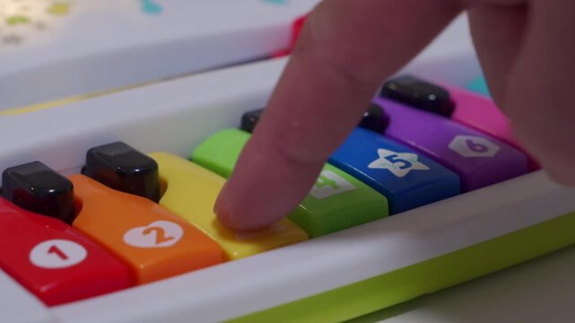 A finger plays up and down the colorful keys of a plastic toy piano. Each note sounds like a cow mooing, creating an ascending and descending musical scale of moos.