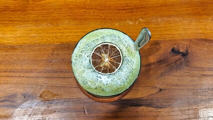 A top shot of a matcha latte in a unique cup, garnished with a dried citrus slice, set on a wooden surface.