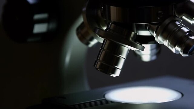 A static macro shot of a microscope objective lenses and stage with a subtle flickering led illuminator light concept of anticipation and scientific observation