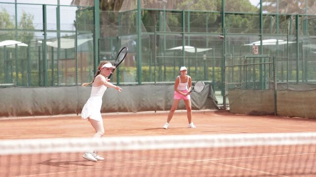 Female athlete plays tennis on open court with girl opponent. Player hits ball with racket, serves ball, and practices actively. Active weekends, outdoor physical activity 