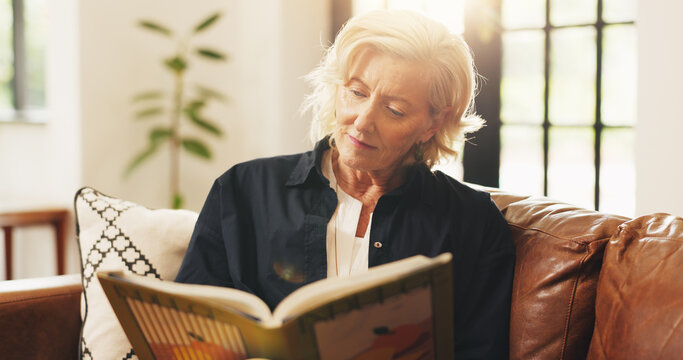 Senior woman, reading book and happy on couch, relax or literature in living room at apartment. Elderly person, smile and novel on sofa for learning, poetry and story with flare in retirement home