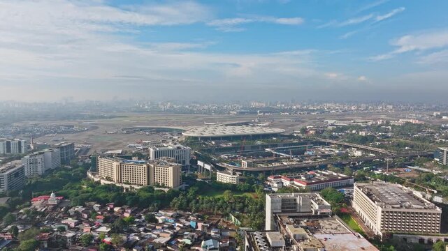 Cinematic 4K aerial dolly-in drone shot of Mumbai International Airport with city skyline in the background under a bright blue sky on a clear day