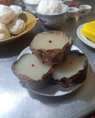 Close-up of traditional Chinese New Year cake (nian gao) placed on a white plate, each wrapped in dry banana leaf with a red dot. The glutinous rice dessert is known for prosperity and good fortune