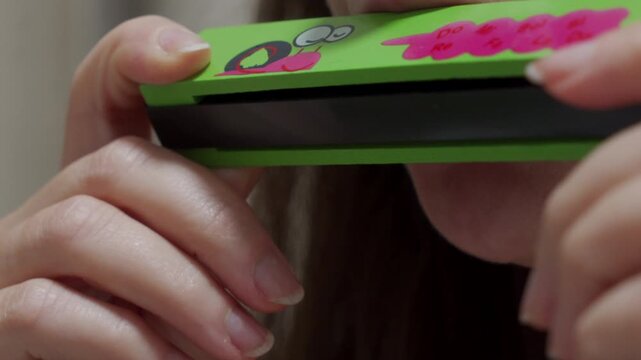 A person plays a green, wooden children's harmonica, decorated with a cartoon snail. The instrument produces a simple, cheerful melody.
