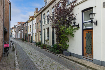 Fototapeta premium A narrow, historic cobblestone street in Zutphen, Netherlands, lined with charming traditional Dutch townhouses and classic street lanterns.