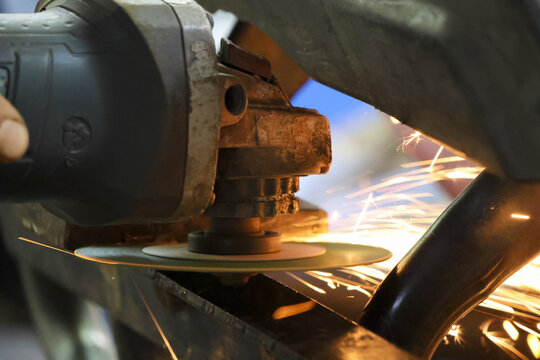 Close up of focused worker grinding metal with an angle grinder power tool. bright hot spark flies from industrial cutting process in metalworking workshop
