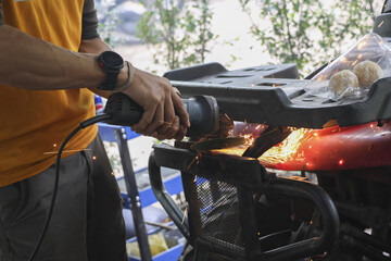 Concentrated mechanic working with power grinder tool on motorcycle. This worker grinds metal, creating bright hot sparks in garage workshop during repair