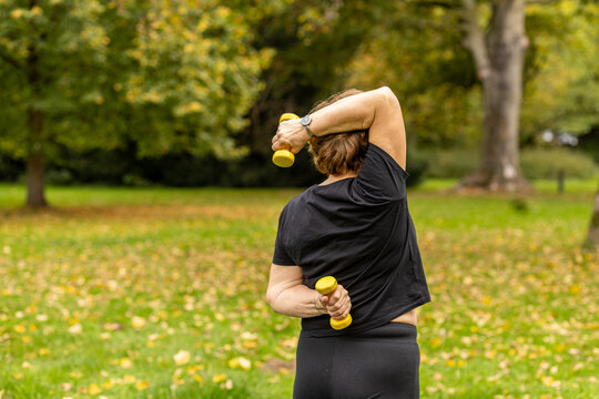 Elderly woman exercises with dumbbells in a park during autumn afternoon in a calming outdoor setting