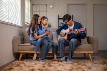 Asian family enjoying music at home, father playing guitar